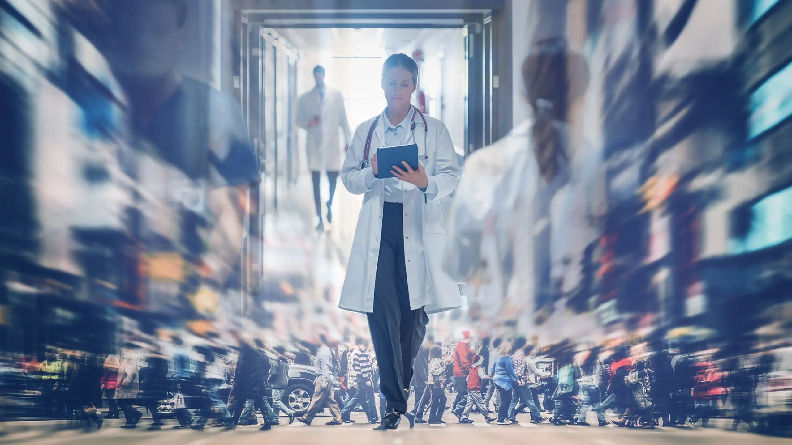 Doctor with tablet in a hospital hallway, blurred crowd reflecting a large, distinct population.