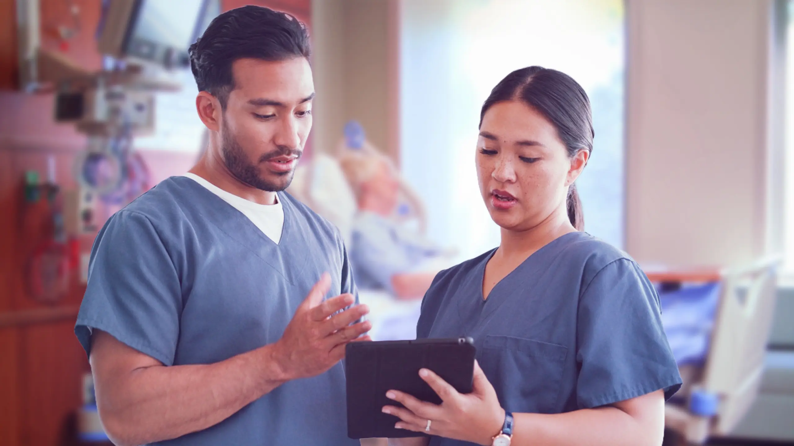 Two nurses in scrubs review patient status on a tablet, weighing observation vs. inpatient decisions at the bedside.
